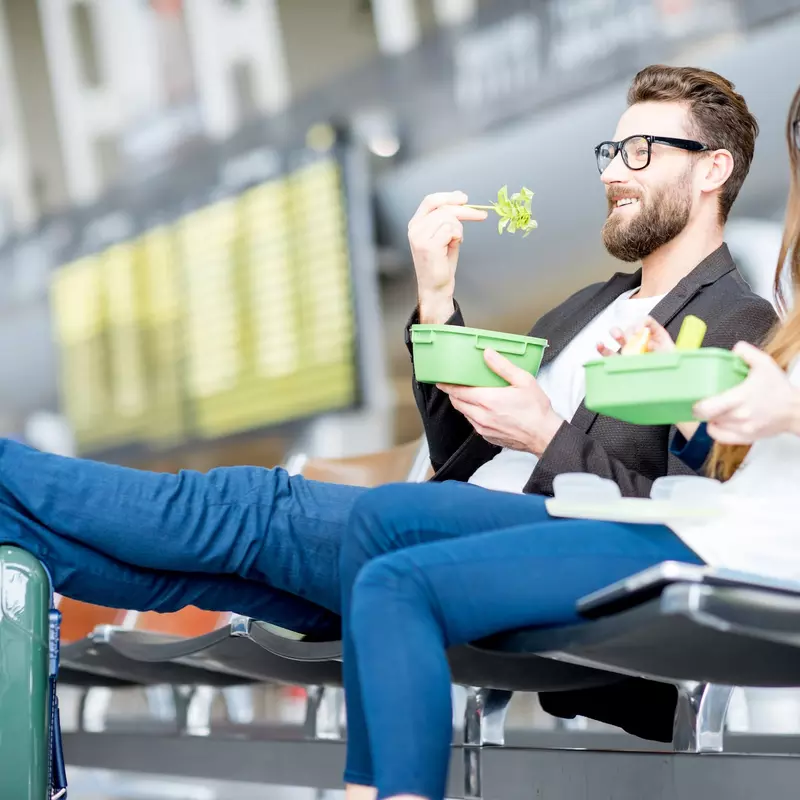 A young couple sitting in the airport lounge, eating healthy meals.