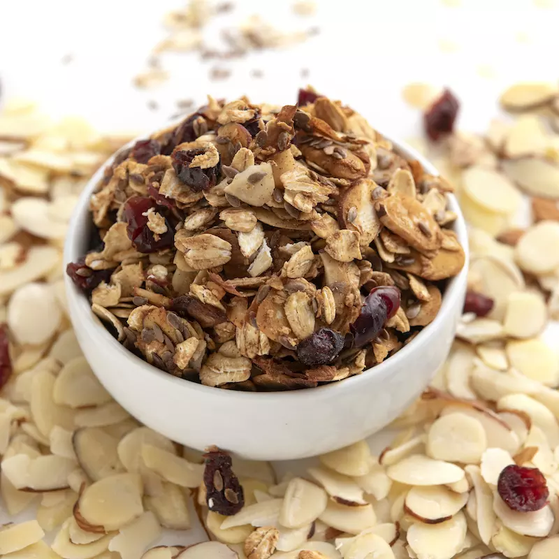 White bowl of granola surrounded by sliced almonds