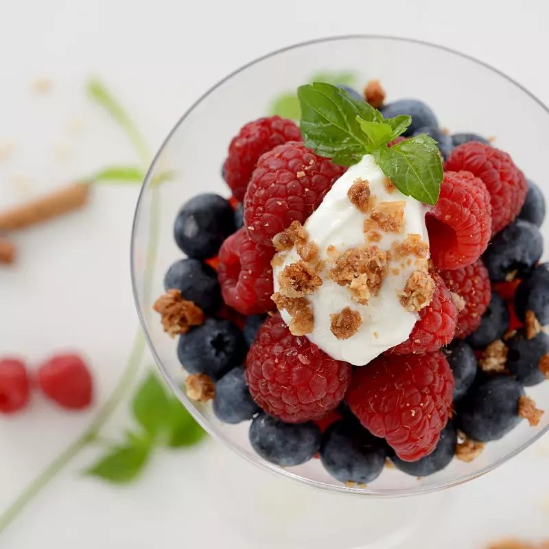a clear glass bowl filled with creamy yogurt and a mix of berries, granola and topped with mint leaves