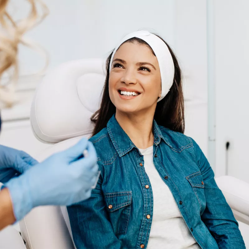 A woman smiles at her healthcare provider before getting a facial treatment.