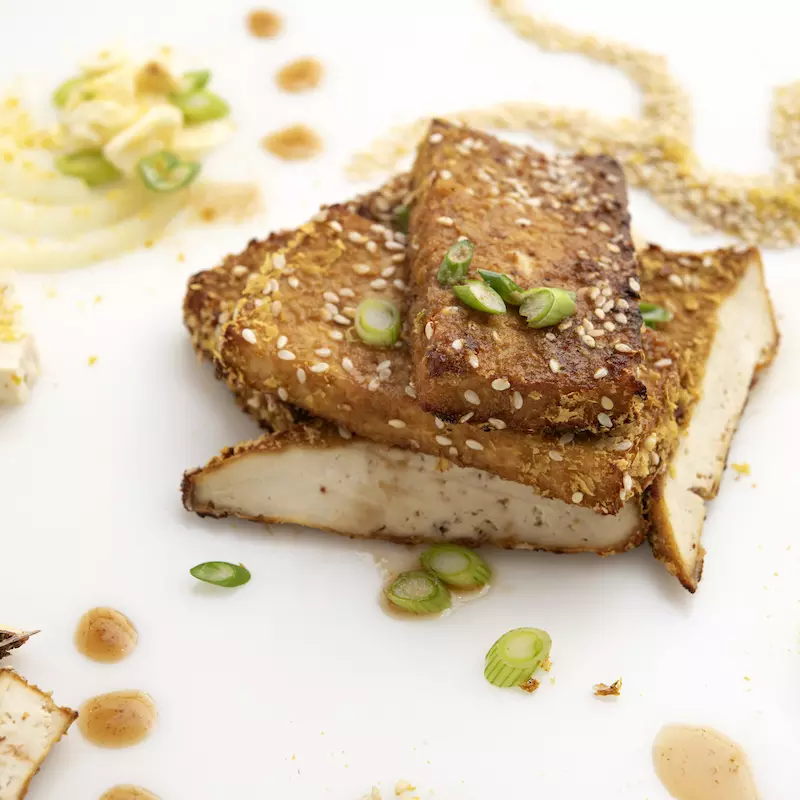three tofu steaks on white surface with nutritional yeast garnish