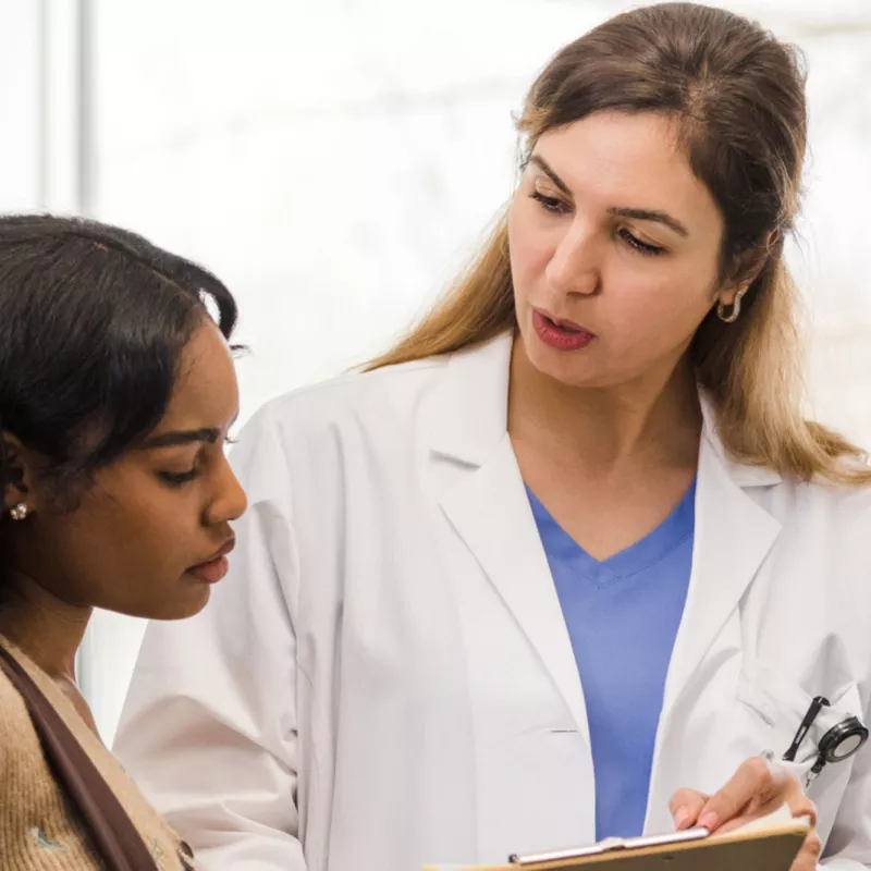 A young woman looks at a clipboard with her female doctor.