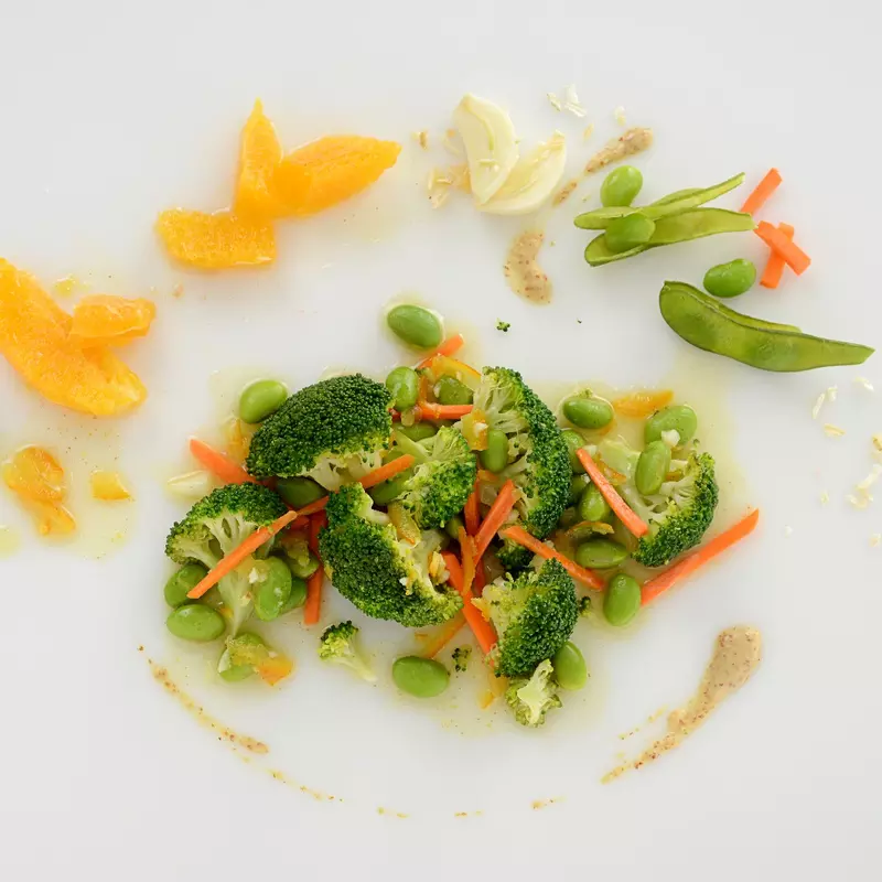 Broccoli, edamame, and shredded carrots, surrounded by orange slices and garlic