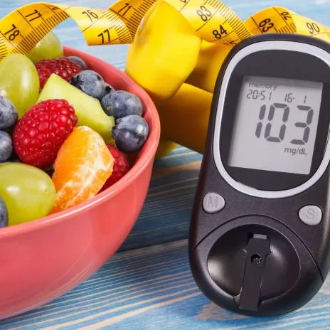 A Bowl of Fruit and a Glucose Checker Lay on a Countertop 