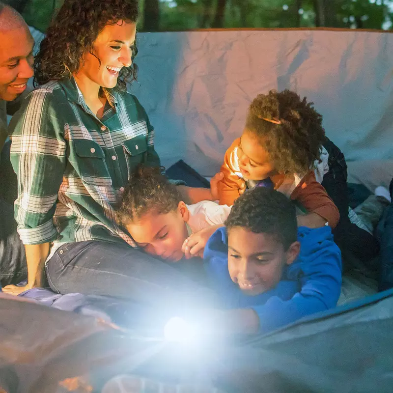 A family of five is snuggled together in a tent with a flashlight on.