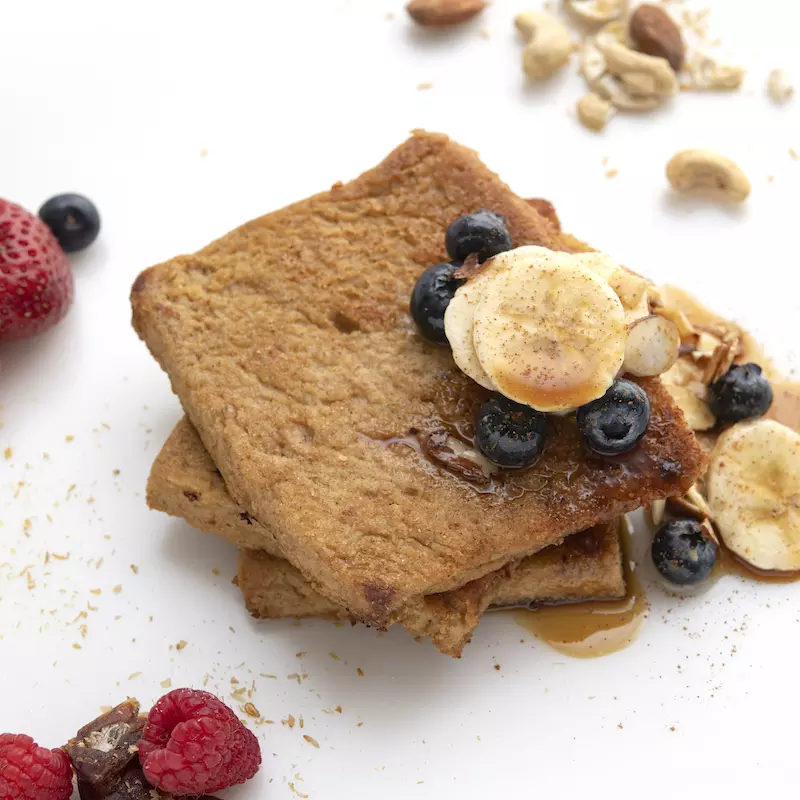 Three stacked slices of French toast with banana and berry garnishes