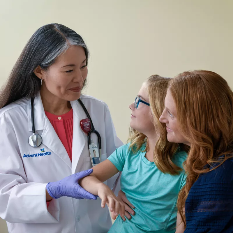 A Physician Checks Her Child Patient's Elbow While Her Mom Comforts Her