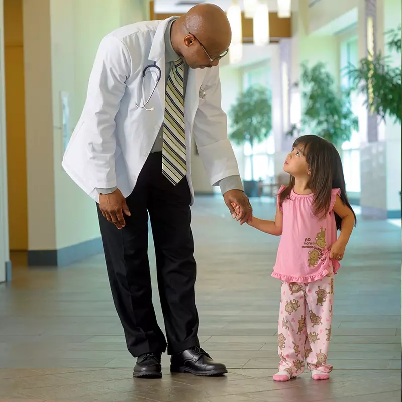 A small girl holds her physician's hand in the hallway.