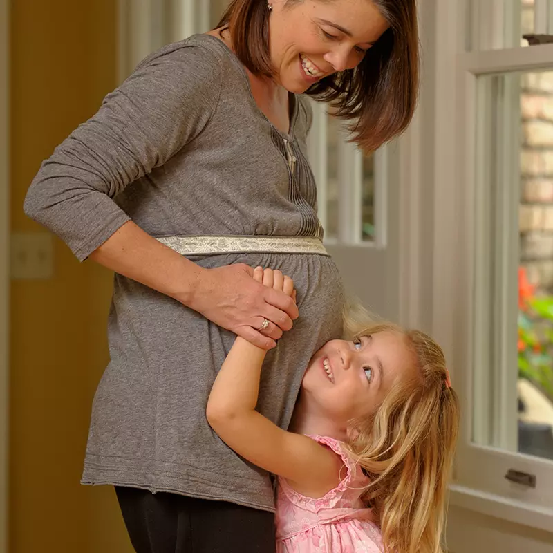A young girl touches her pregnant mom's belly.