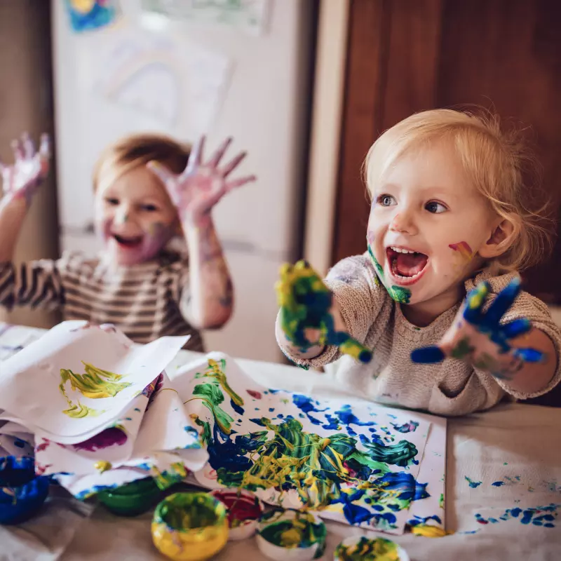 Children finger painting with paint on their hands and clothes