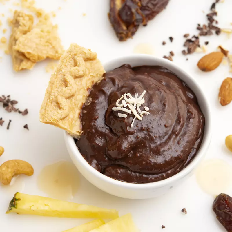 Carob pudding in bowl with a pie crust garnish, surrounded by decorative nuts