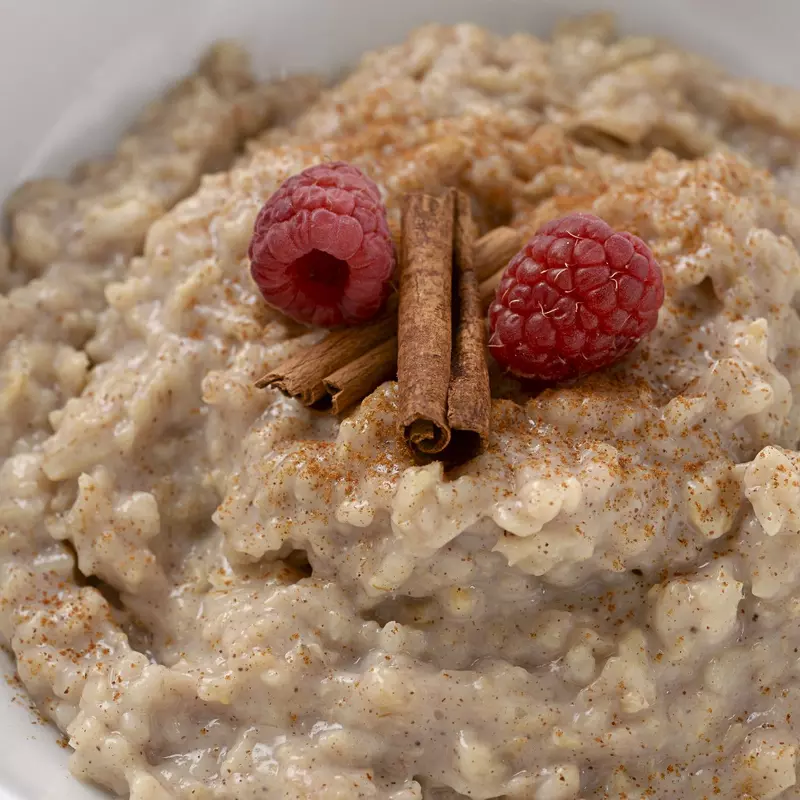 a bowl filled with a sweet cinnamon oatmeal mixture, topped with two raspberries and a cinnamon stick
