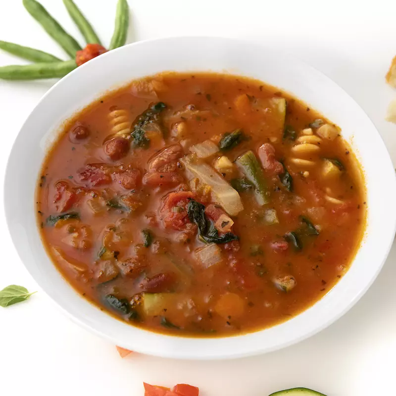 Bowl of minestrone soup with greens and mushroom garnishes