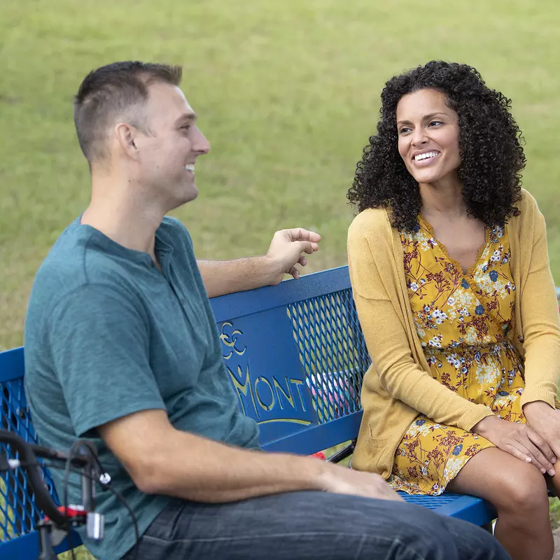 Couple sitting on a bench in a park smiling at each other