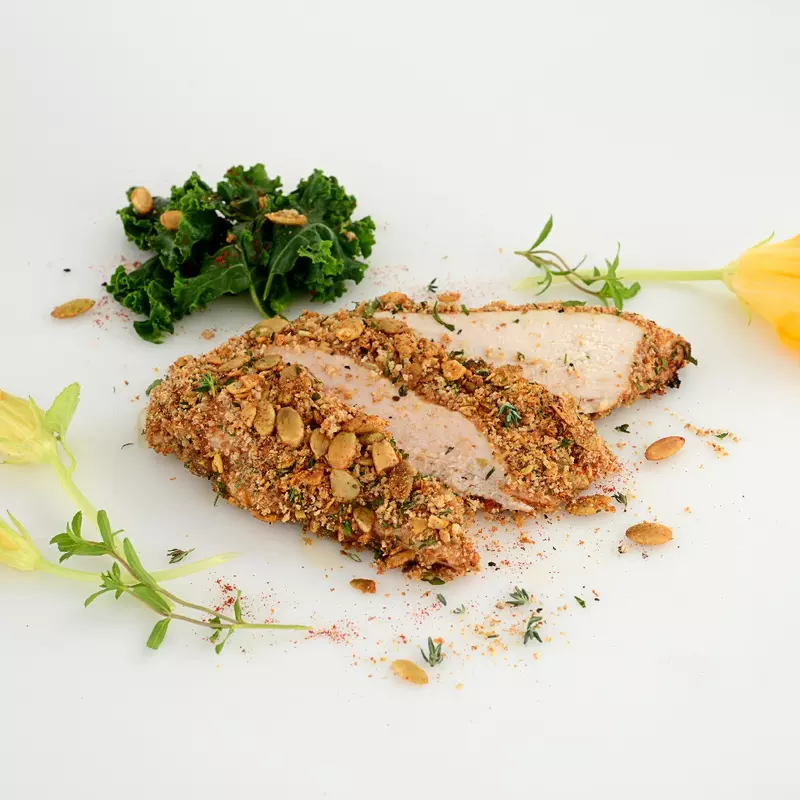 a serving of chicken, coated in a pumpkin seed crisp, sliced into three pieces