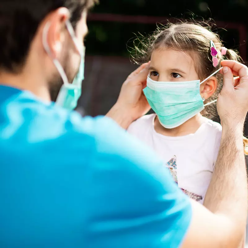 Father putting mask on daughter outdoors