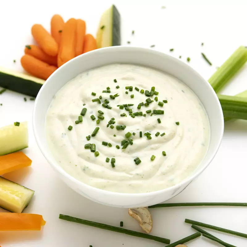 Bowl of sour cream surrounded by vegetable sticks.