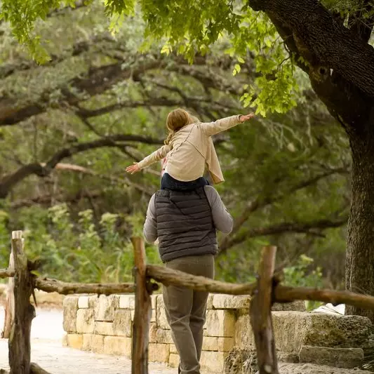 A dad walks through the trees with his daughter on his shoulders