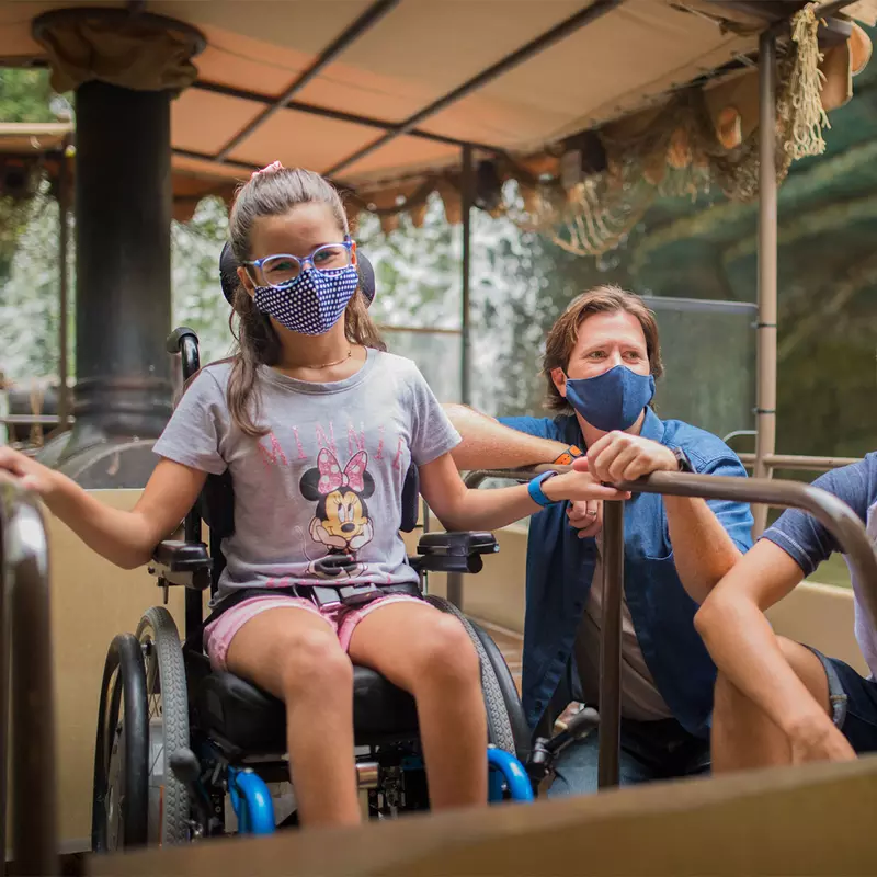 A young girl in a wheelchair and wearing a mask while riding Disney's Jungle Cruise ride.