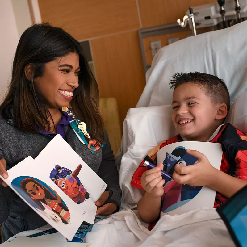 Boy looking at a Disney Team of Heroes Care Package with an AdventHealth for Children staff member.