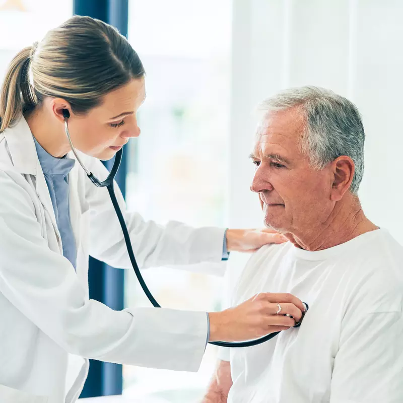 Doctor checking an older male patient's lungs with a stethoscope.