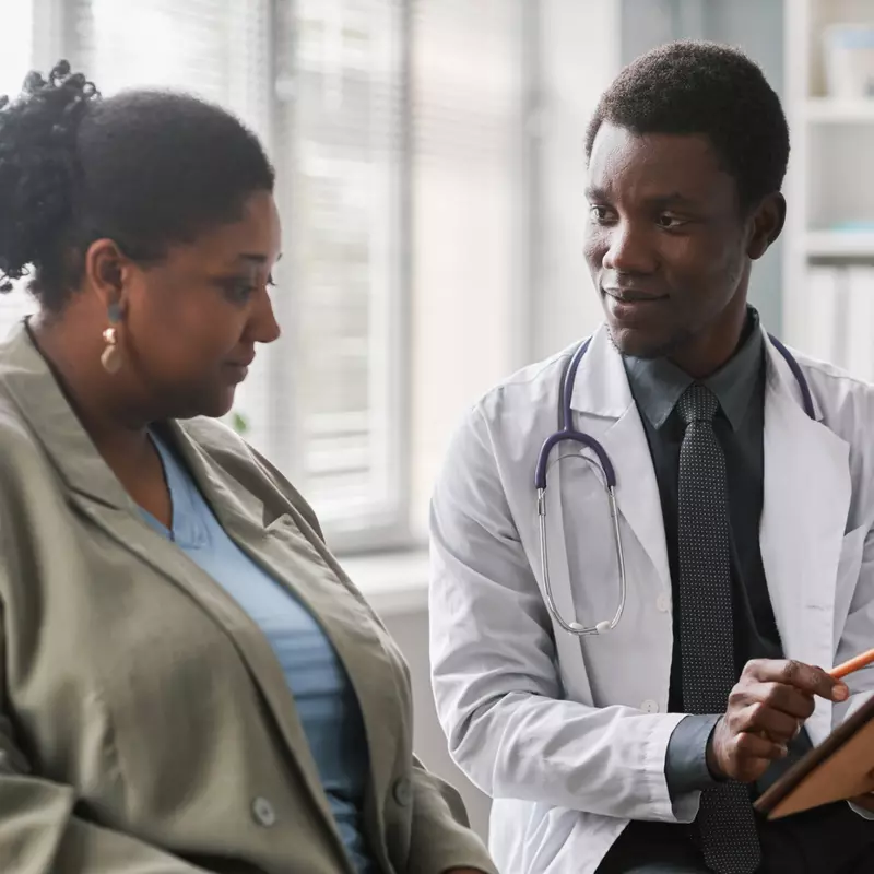 A black woman patient talks with a black male doctor.