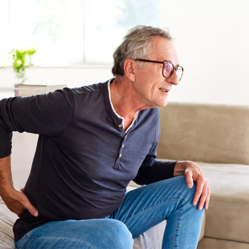 Older man holding his back with his hand while getting up off the couch.