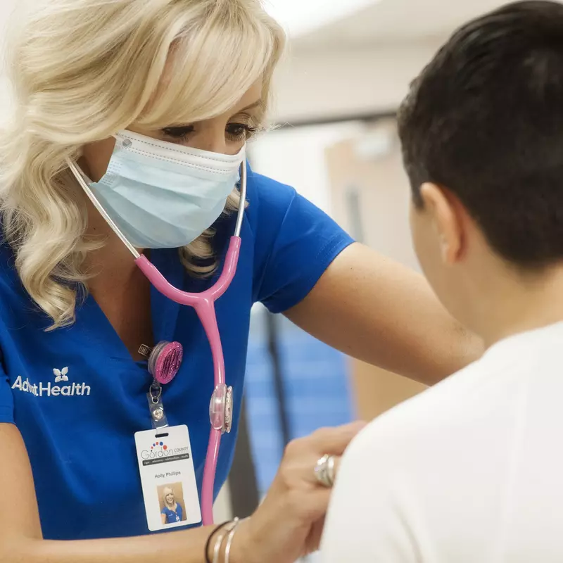 An AdventHealth employee using a stethoscope on a young teenager