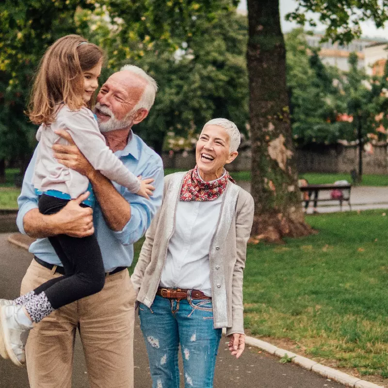 An older couple walking in the park, holding their granddaughter