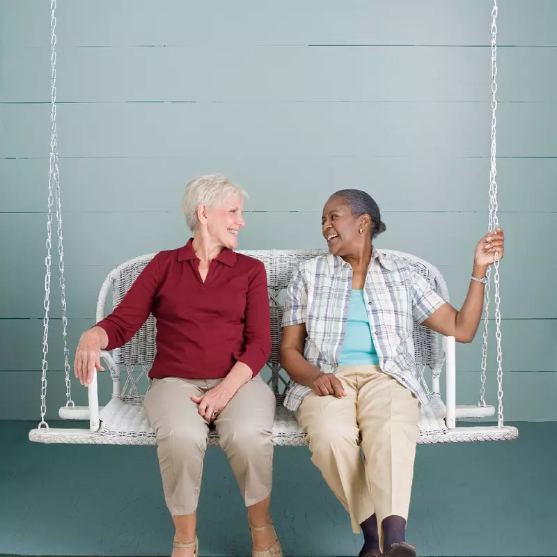 Two older women sitting on a porch swing.