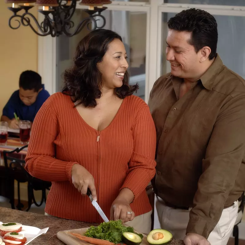 A Hispanic couple prepares a healthy meal for their family in the kitchen.