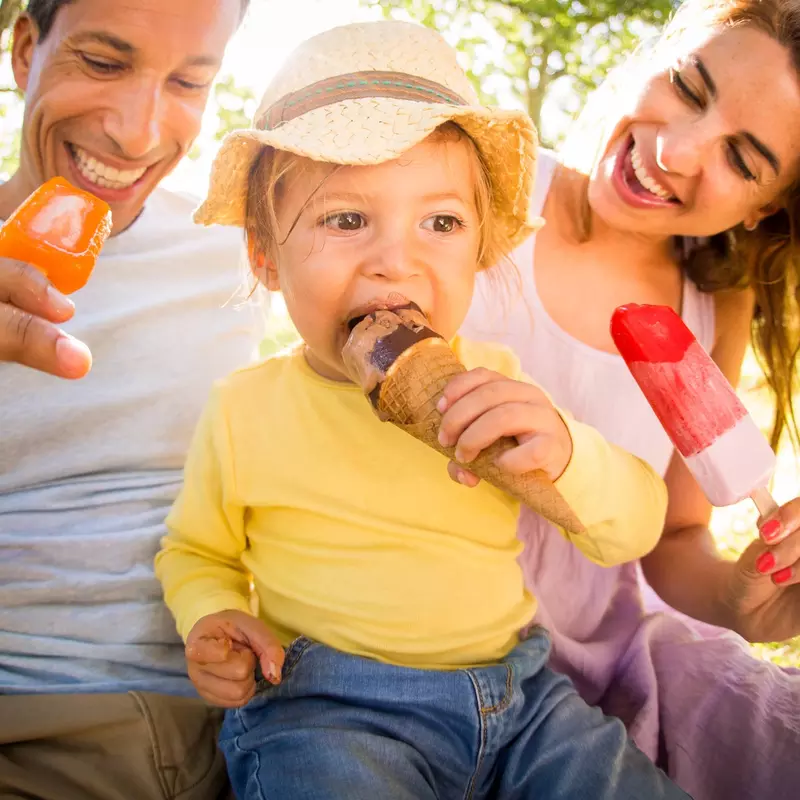 Family of three, sitting on the ground eating popsicles
