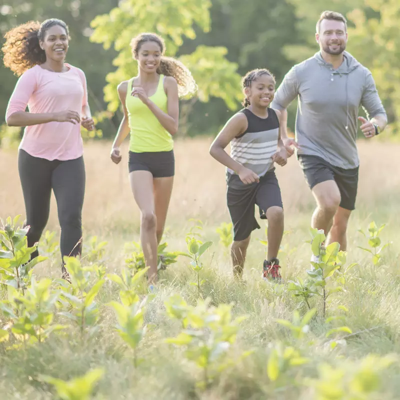 A family of four, running together outside in a field.
