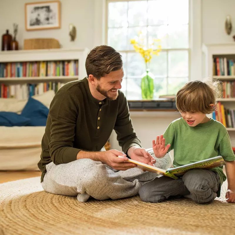 A dad reading a book to his little boy in the family room.