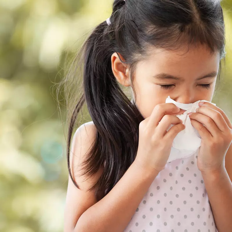 A little girl blows her nose into a tissue.