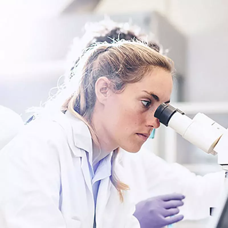 A female lab technician looking through a microscope.