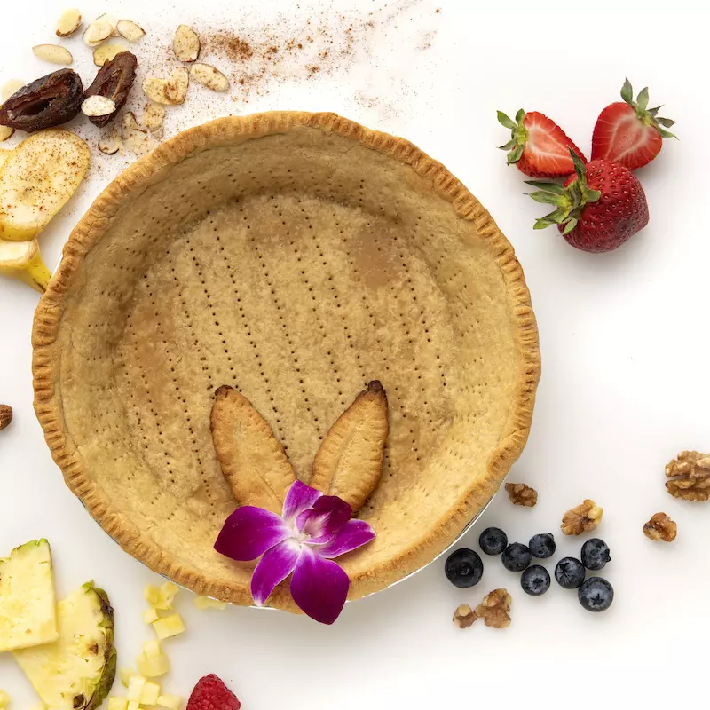 Whole, empty pie crust decorated with fruit chunks and an orchid.