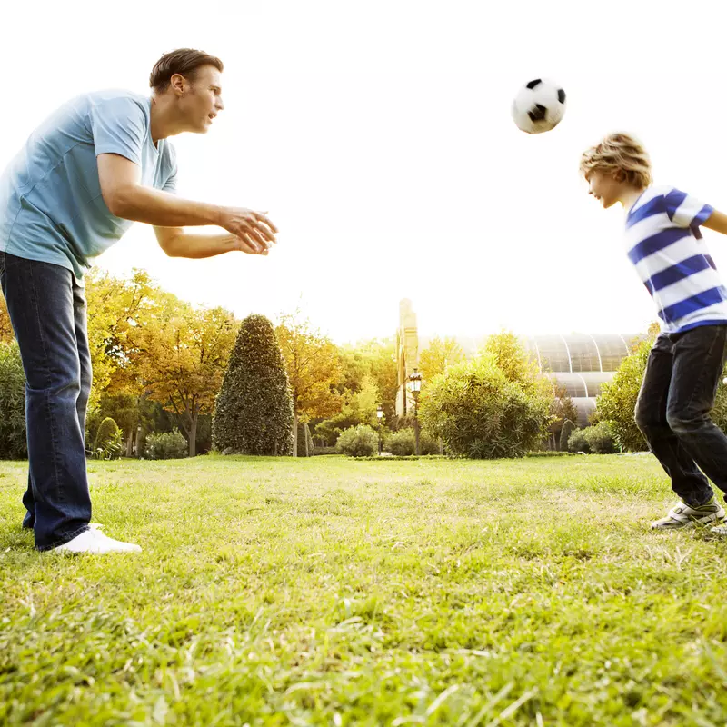 Father and son play soccer in the yard.