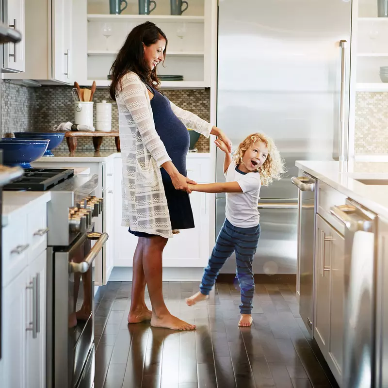 A pregnant woman and her daughter stand in a kitchen.