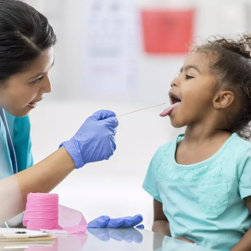 Little girl sitting on her mother's lap sticking her tongue out for the doctor.