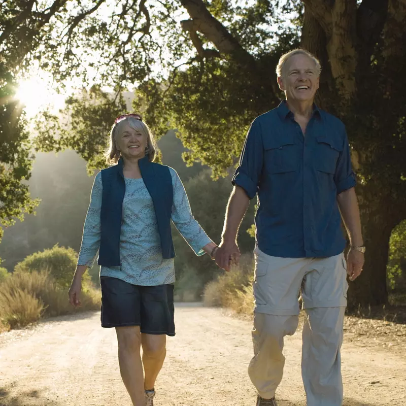 An older Caucasian couple takes an evening walk on a trail.