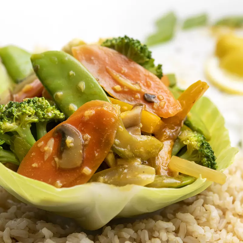 Lettuce bowl filled with veggie stir-fry sitting on brown rice