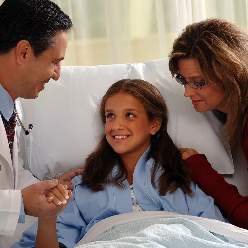 A young patient with her mom holds the hand of her doctor.