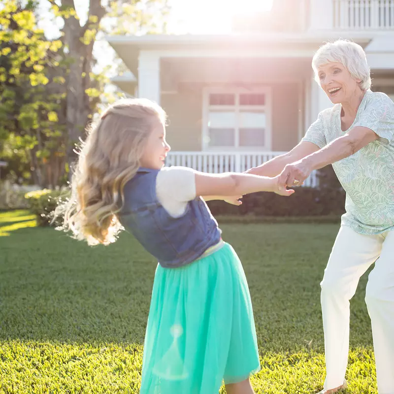 A grandmother whirling with her grand-daughter in the backyard.