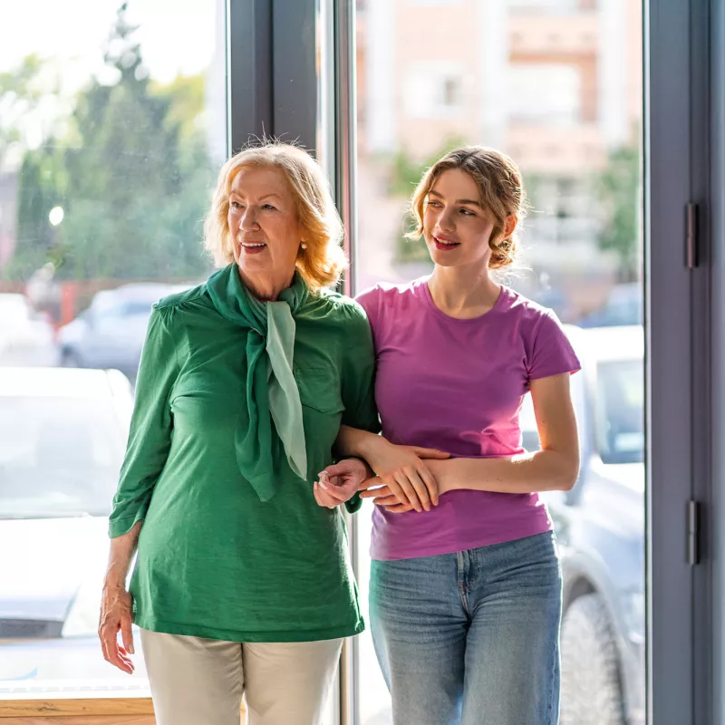 A grandmother and granddaughter walking into a hospital or medical clinic.