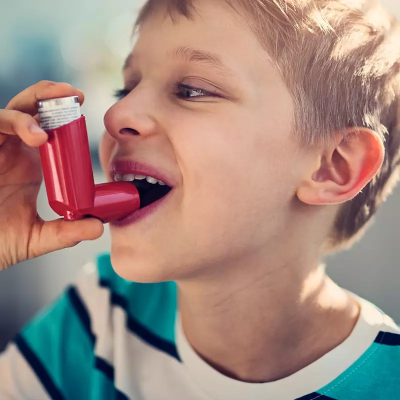 Young boy smiling about to take a puff from an inhaler.