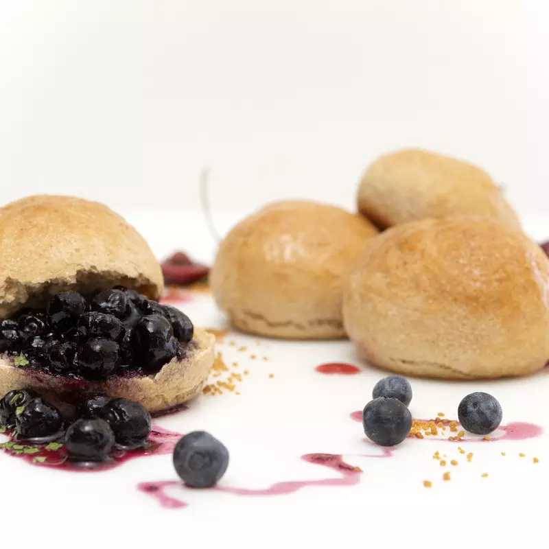 four fresh baked rolls, one covered in blueberries with a fruit syrup