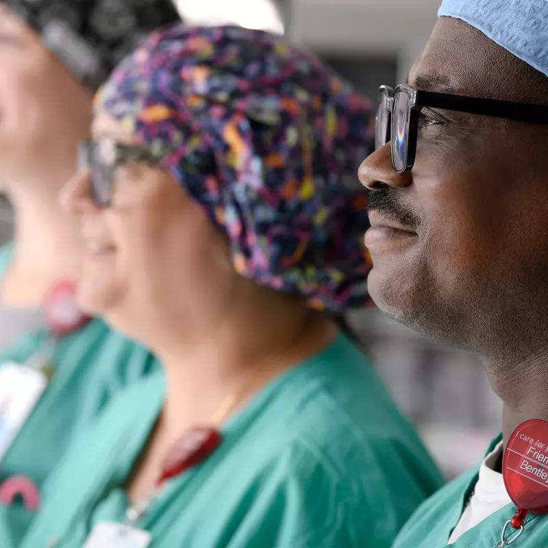 Three surgical nurses stand in the OR and look hopefully to the left of the image.