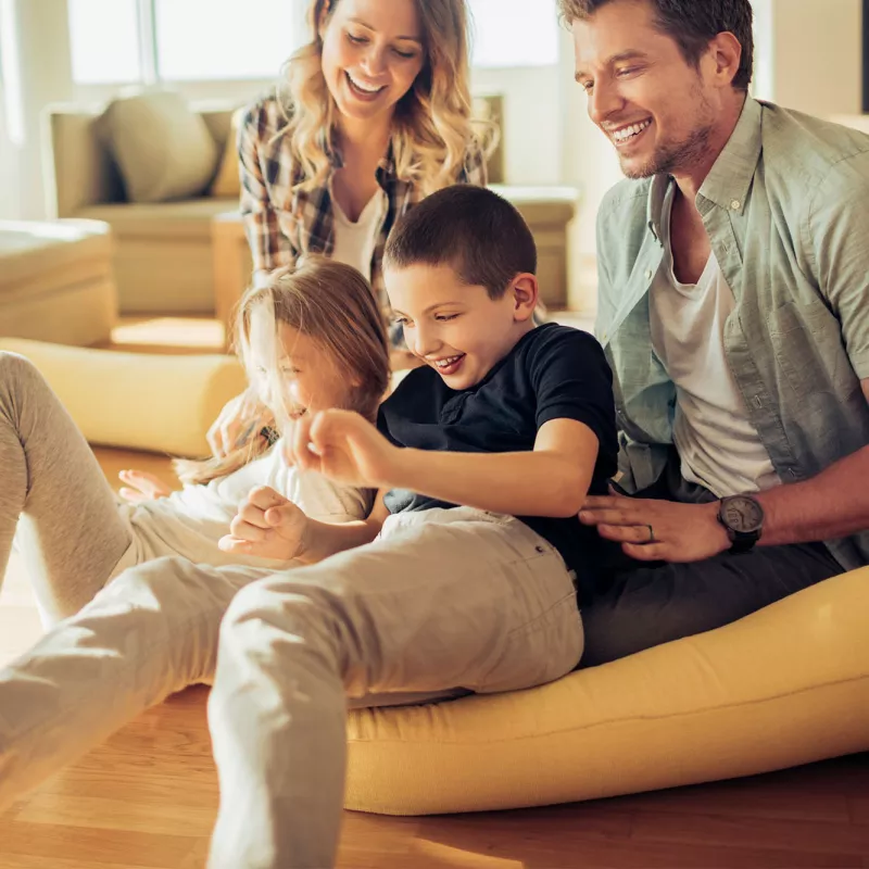 Family playing and laughing together in a sun filled living room of their house.