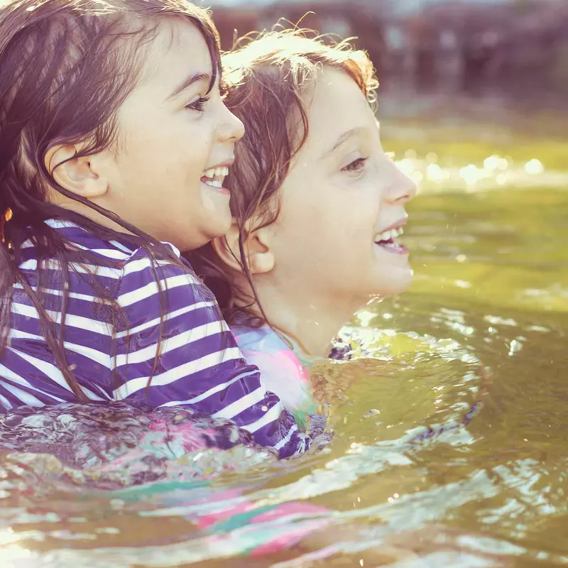 Two young children, one holding the other, swimming in a lake.
